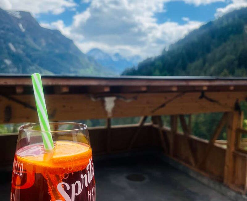 Aussicht von der Terrasse auf die Bergwelt mit einem Aperolspritzer im Vordergrund